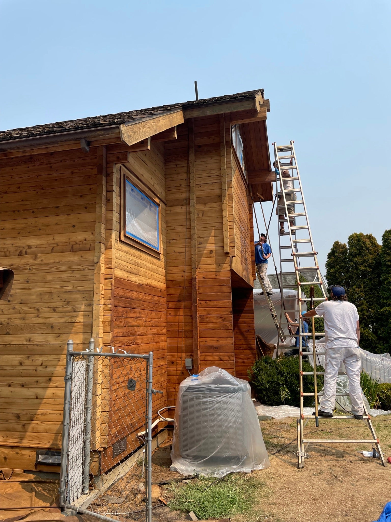 A crew of 3 men staining a cedar log home together using Lovitt's Emerald Gold log home stain in NATURAL color